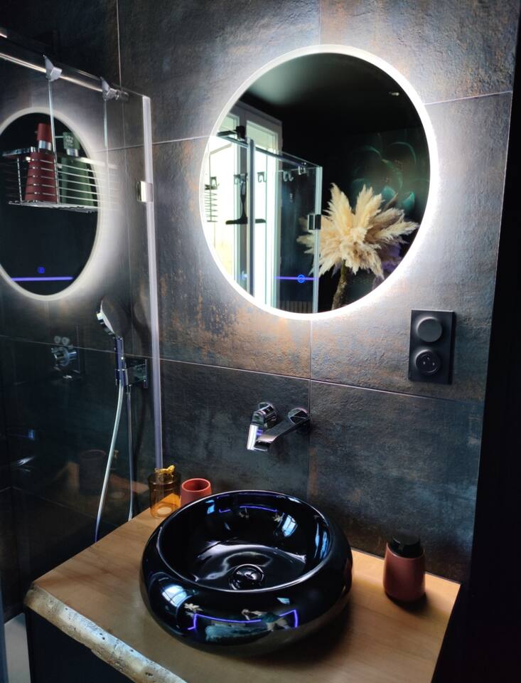 Salle de bain design avec grand miroir circulaire LED, vasque noire et douche à l'italienne